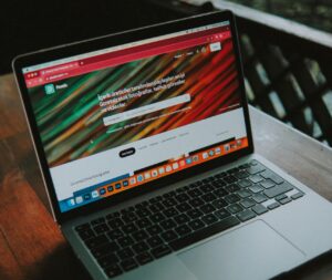 A close-up view of a laptop with a website open, placed on a wooden table near a window.